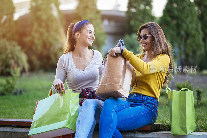 两个妇女坐在城市公园，看购物袋后，购物