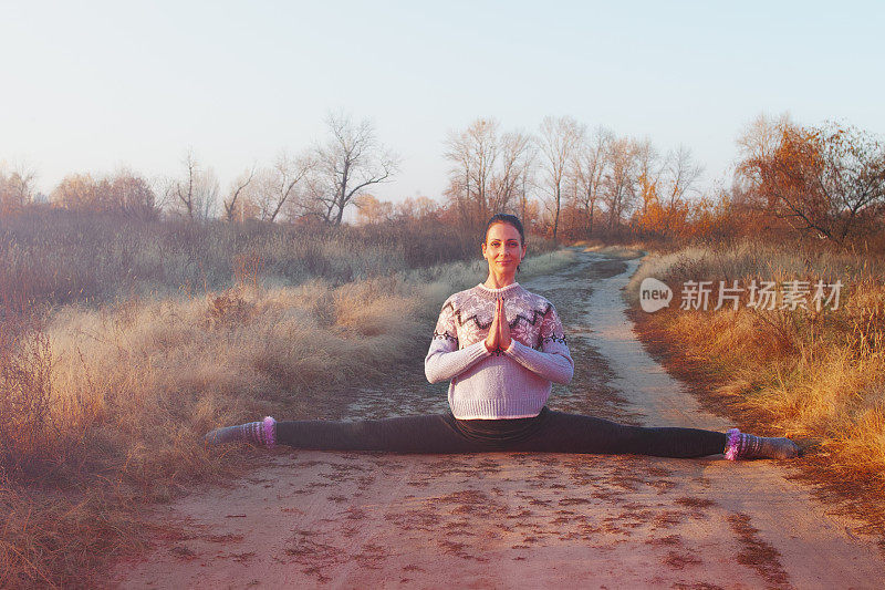 年轻的黑发女子在秋天的森林里练习瑜伽在日落