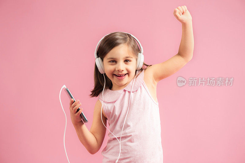 在粉红色背景下听音乐跳舞的小女孩