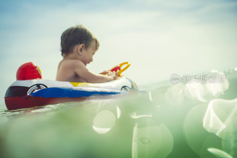 小男孩坐在充气木筏上，在海上享受海滩假日