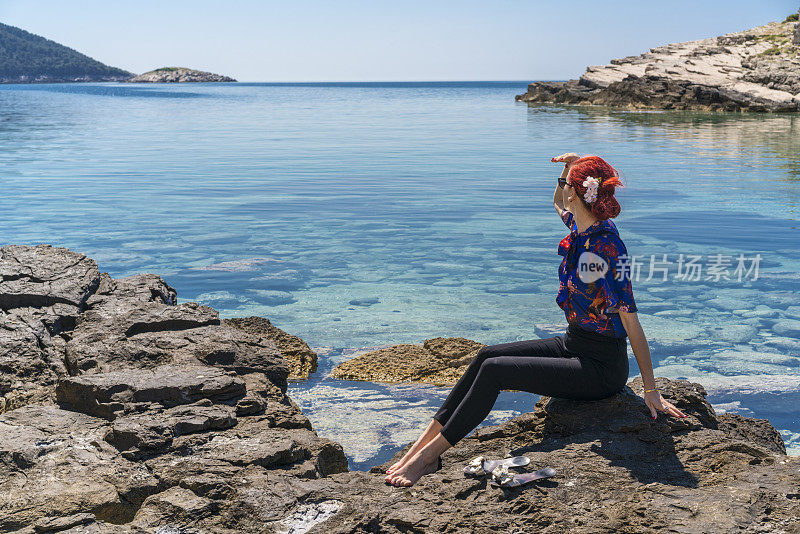 年轻美丽的女人坐在靠近大海的岩石上，在克罗地亚Mljet岛眺望大海