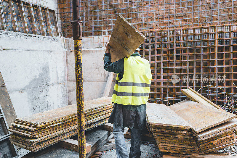 建筑工人正在建筑工地搬运一块木板