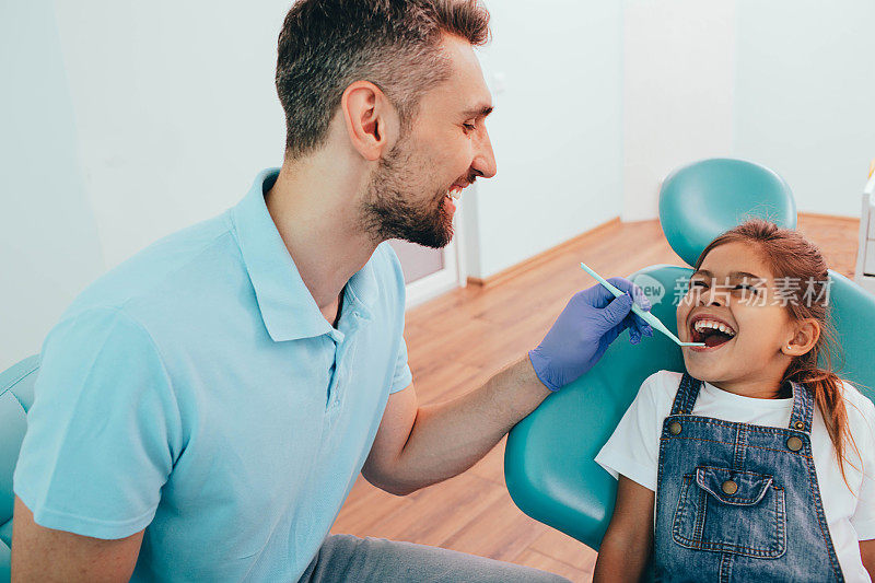 嘿，让我看看你的牙齿。男牙医在牙科诊所给一个小女孩检查牙齿