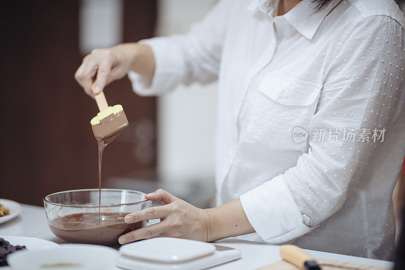 一名亚裔华人女沙漠厨师在家中准备巧克力松露，混合和报废巧克力