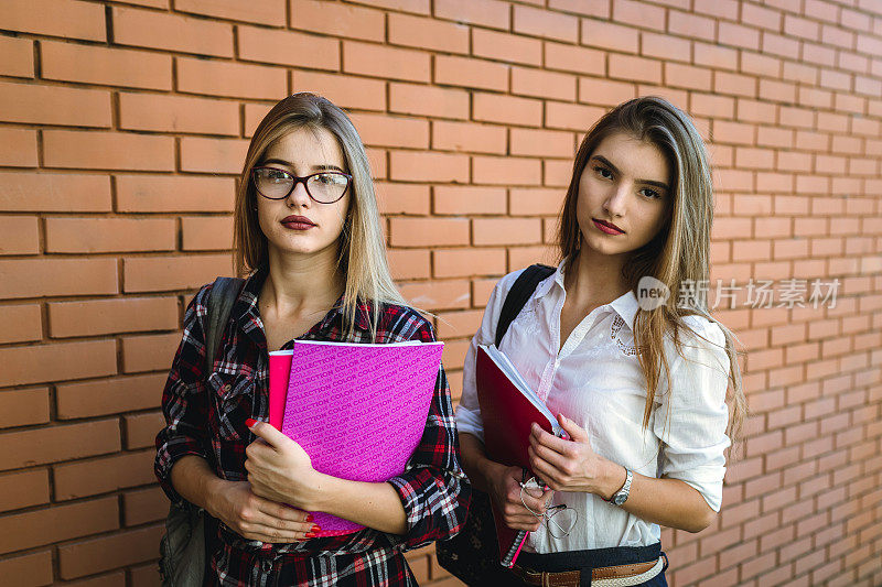 两个十几岁的女学生拿着书在校园里