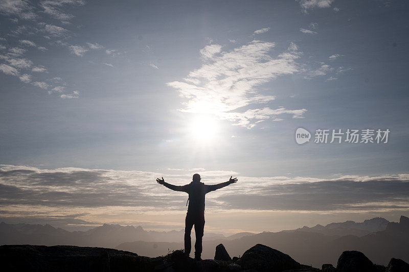 男性徒步旅行者在日出时举起手臂站着