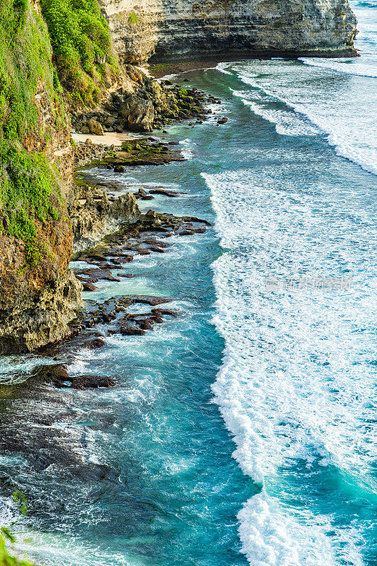 Uluwatu巴厘岛。蓝色的海洋和岩石山，覆盖着热带树木。