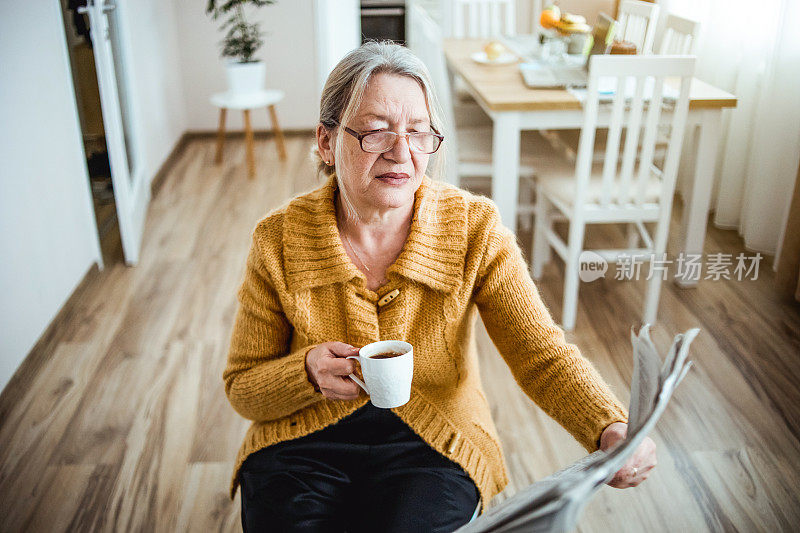 一位老妇人在家里看报纸，喝咖啡