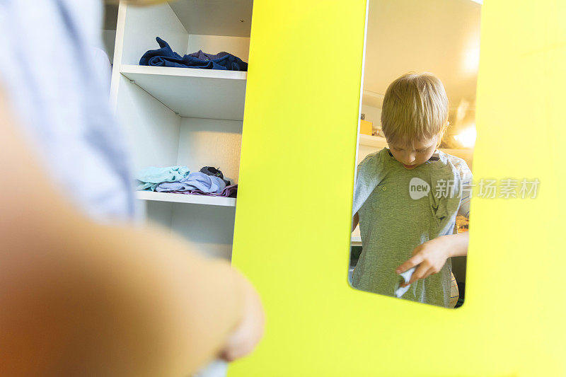 7岁的小男孩看着镜子，拆开自己的衣服。在冠状病毒大流行期间呆在家里。