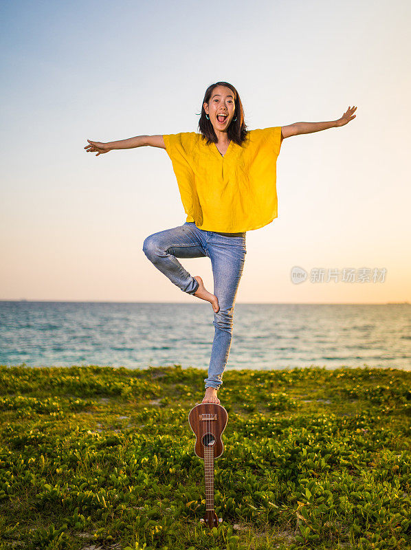 年轻快乐的女人在海边用她的尤克里里琴保持平衡