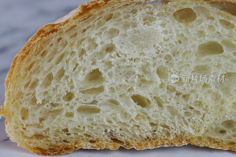 这是自制的脆皮意大利面包片的特写图像，显示出纹理的细节，金黄色，刚出炉的烤箱，硬面包切成薄片，大理石效果的背景