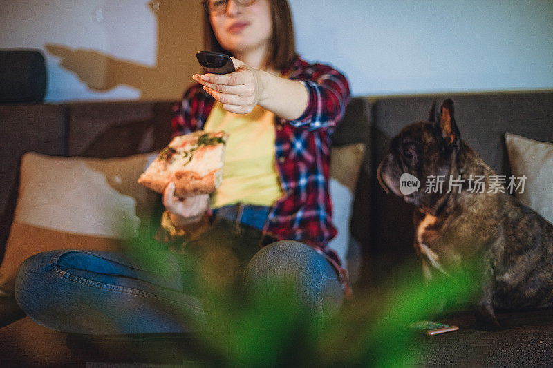 一个女人在沙发上吃披萨，和她的狗一起看电视