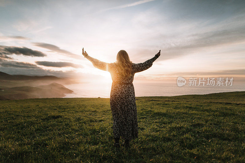 夕阳西下时举起双手的年轻女子