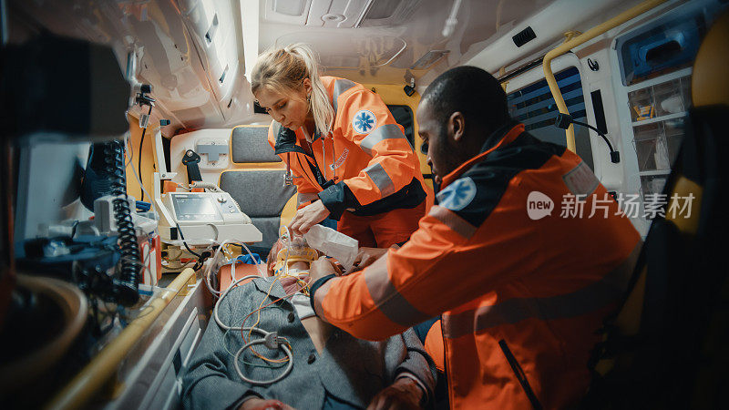 女性和男性EMS护理人员提供医疗帮助受伤的病人在去医疗保健医院的路上。急救助理在救护车上戴上无创通气面罩。