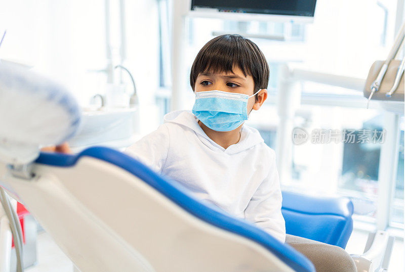 一位戴着防护口罩的小男孩病人正在牙科诊所等候牙科治疗。