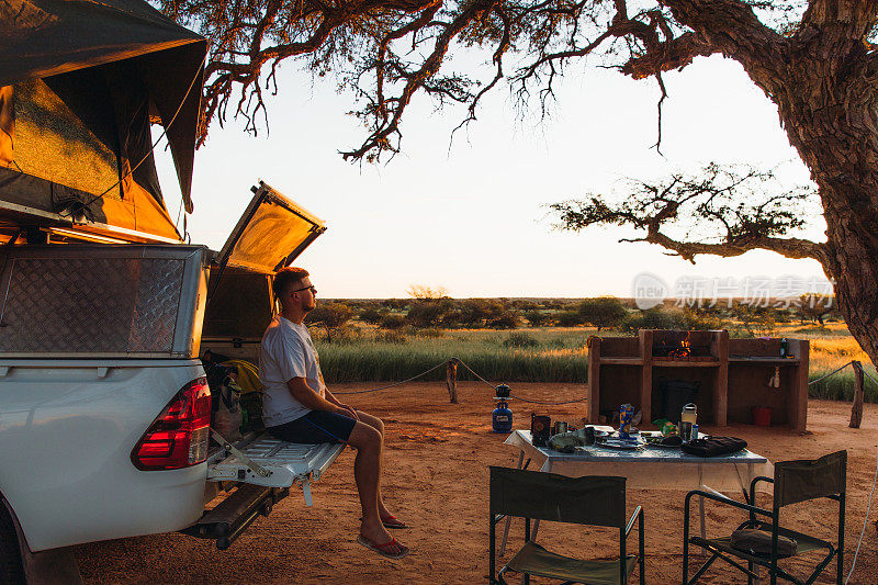 纳米比亚喀拉哈里沙漠，一个年轻的旅行者坐在露营车上欣赏美丽的日落
