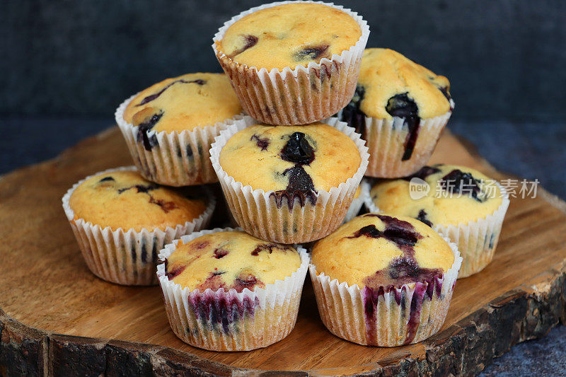 特写图像蓝莓松饼堆在纸蛋糕盒上木质蛋糕架，斑纹的黑色背景，聚焦前景