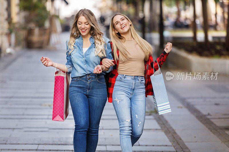 年轻的女性朋友们拿着购物袋走在市区里。