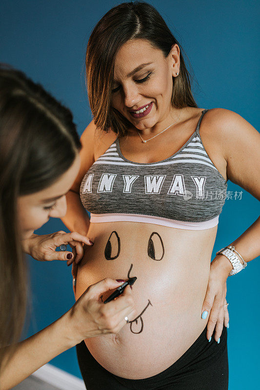 怀孕的女人正在画她怀孕闺蜜的肚子