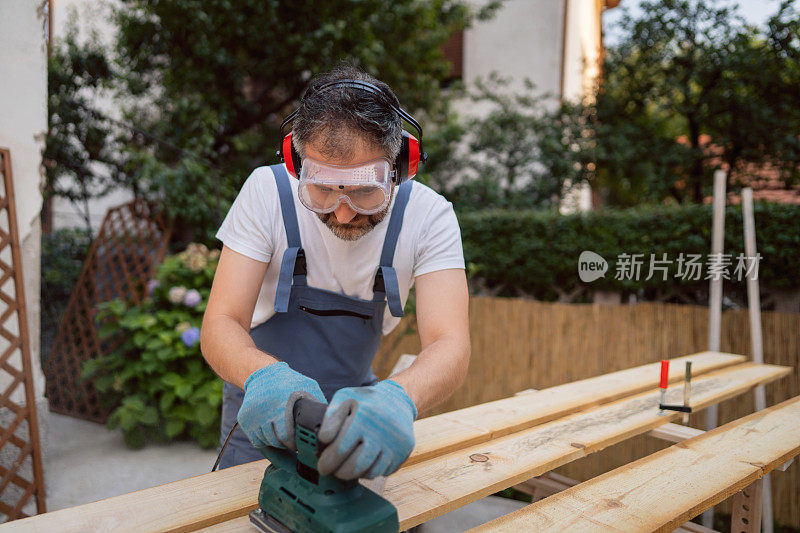 在室外车间，熟练的木匠用砂光机打磨木材表面