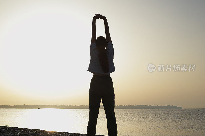 年轻女子在海边做晨练，以在日出时保持身材