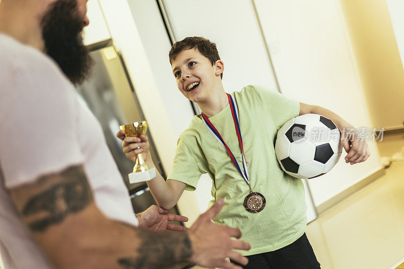 骄傲的父亲感到如此兴奋，看到他的儿子奖牌和奖杯在他的足球比赛后。