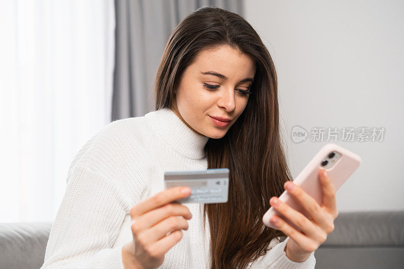 年轻女子持有信用卡和使用手机。