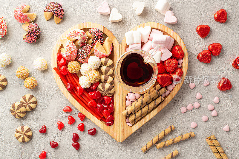 情人节庆祝概念。顶部视图照片木制心形托盘与糖果巧克力果冻糖果饼干和玻璃杯饮料的混凝土纹理背景