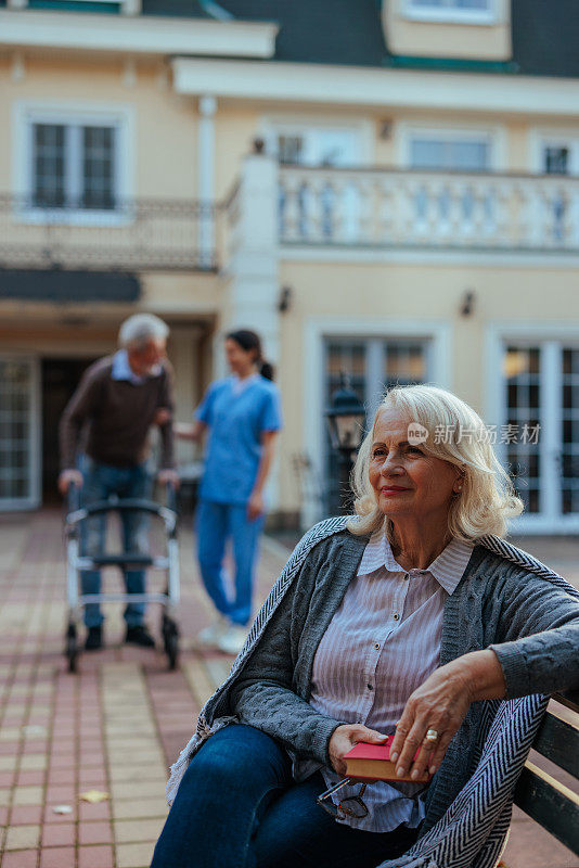 老年妇女坐在养老院的长凳上。