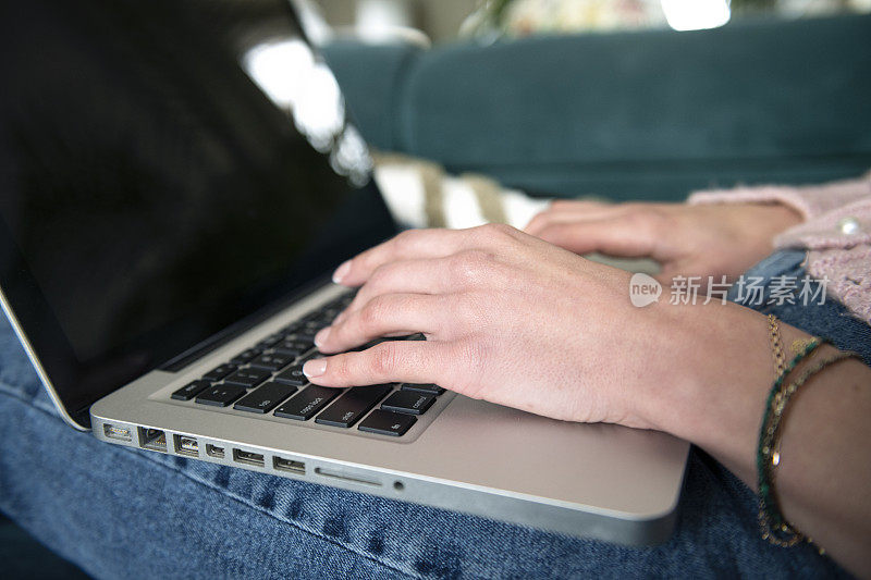 一位女士坐在家里的沙发上，用空白屏幕的笔记本电脑工作和打字