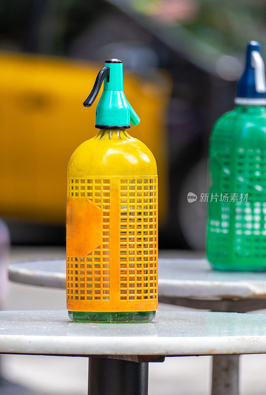 在巴塞罗那一家古色古香的老酒吧的露台上，小圆高桌上的塑料网虹吸着橙黄色和其他老式绿色的苏打水，喝着苦艾酒。