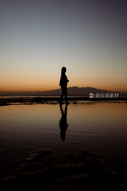 夕阳下，亚洲女孩带着相机走在沙滩上