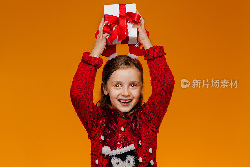 一个穿着红色圣诞毛衣的女孩对收到的礼物很满意，她期待着打开装有珍贵礼物的盒子。