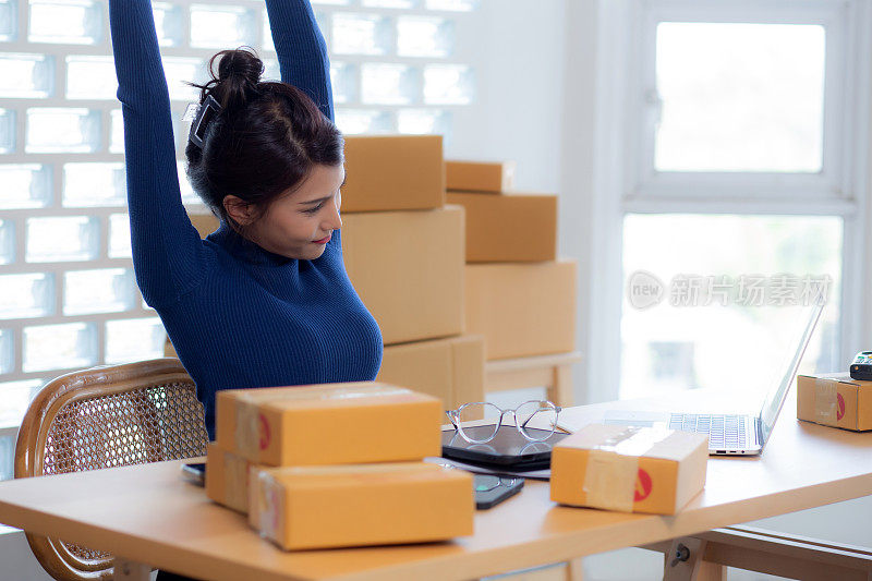 年轻的亚洲女性在网上为卖家提供送货服务，而女性则在家里休息放松，舒展双手，在线送货，自由职业者做小生意或创业和零售。