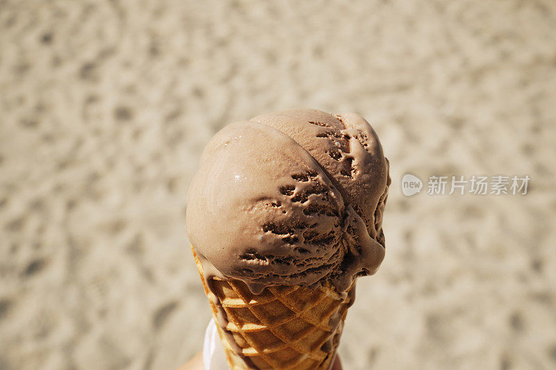 在一个阳光明媚的日子里，坐在沙滩上的巧克力冰淇淋蛋筒上。