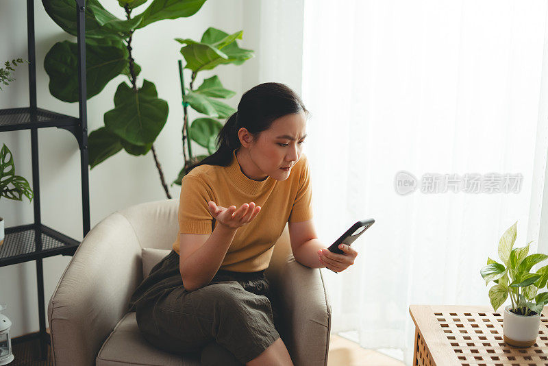 亚洲女性坐在家里看智能手机屏幕，有问题。