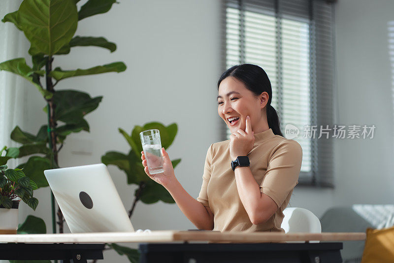 坐在家里办公室喝凉水休息的亚洲女性。