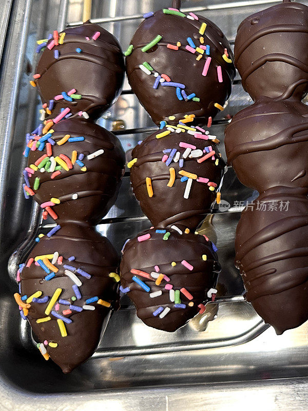 全画幅图片:一排排的木串，每个都有三个黑巧克力覆盖的草莓，装饰着巧克力和糖屑，放在金属托盘架上，玻璃镶板的面包店货架展示，高架视图