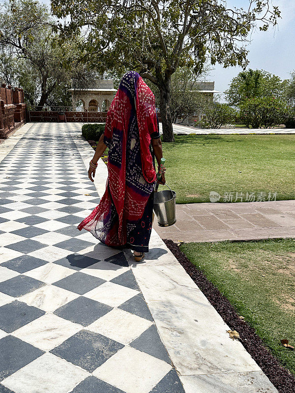 印度妇女穿着传统服装纱丽和帕露，走在黑白格子铺的小路上，单色棋盘图案，后视图，重点在前景