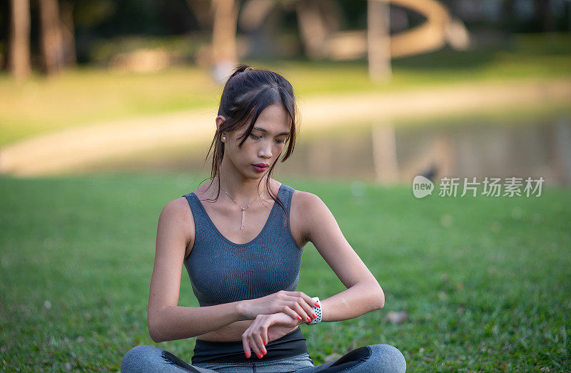 年轻美丽的亚洲女子在城市公园放松，看着她的健身手表后，每天的健身训练。