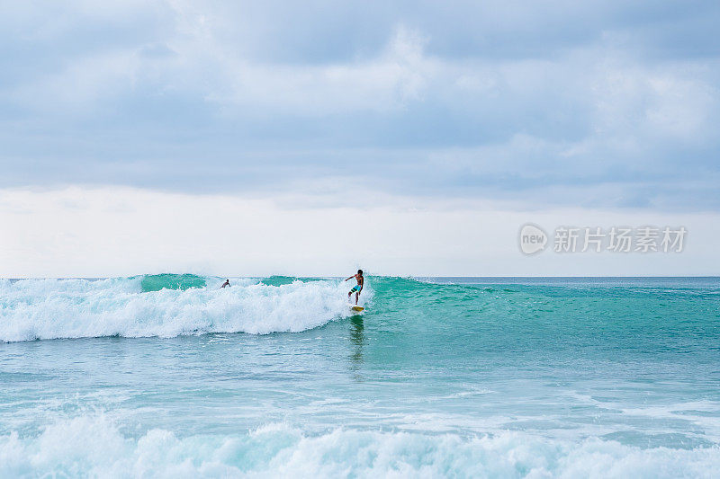 冲浪者骑着绿松石浪:一个熟练的冲浪者在清澈的蓝色海洋中的白色冲浪板上的动态动作镜头。摄于巴厘岛梦幻海滩。