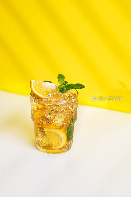 一杯加柠檬和薄荷的冰茶，黄白色的背景上有阴影。