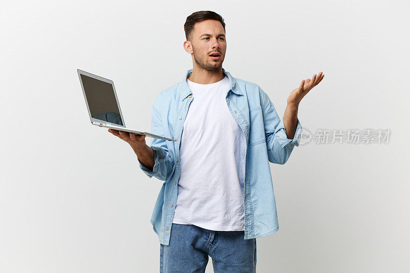 震惊、不开心、皮肤黝黑、穿着休闲基础t恤的英俊男子被糟糕的小玩意惹恼了，笔记本电脑工作在白色的工作室背景上独自摆姿势。复制空间横幅模型。电子维修IT概念