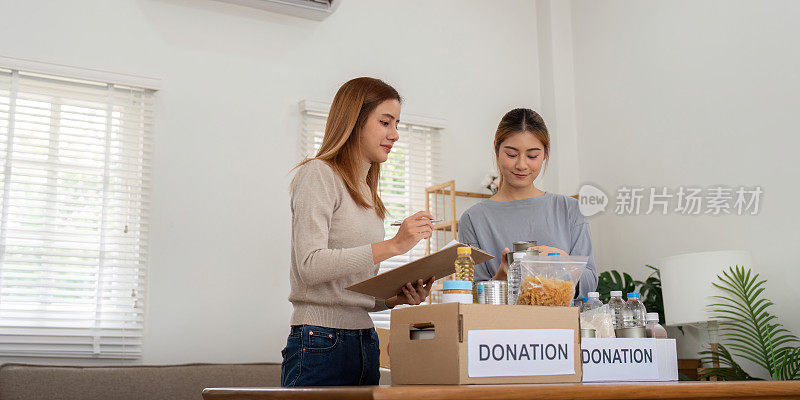 捐赠和两位妇女志愿者快乐地在家里打包食物。慈善机构