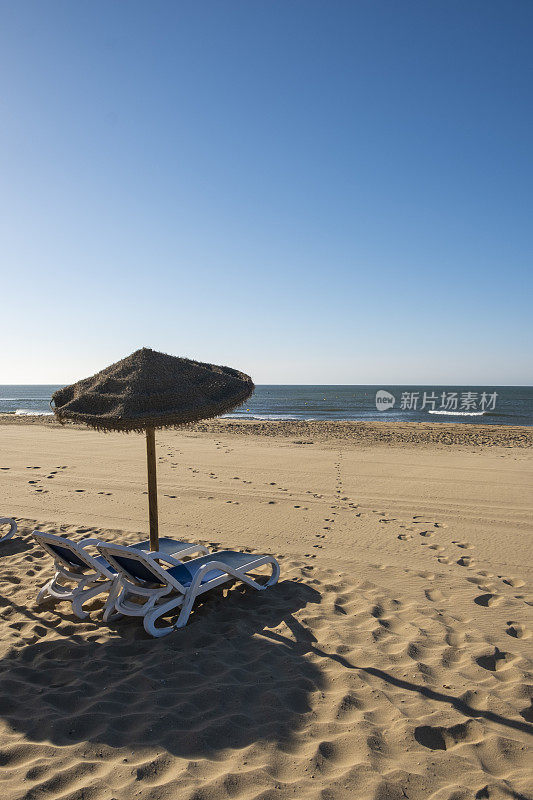 美丽的夏日风景的西班牙海岸，两个太阳躺椅，太阳躺椅和遮阳伞。金色细沙，地平线海景，蓝天，平静放松。鼓舞人心的度假景观。