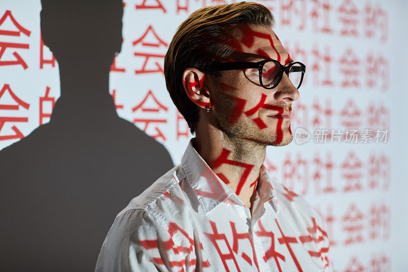 一个自信的年轻人，留着胡茬，站在投影屏幕前，屏幕上写着象形文字，对中国观众的创业项目表示不满