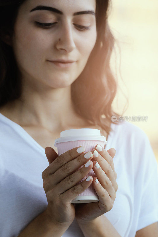 年轻女子拿着热咖啡和手机