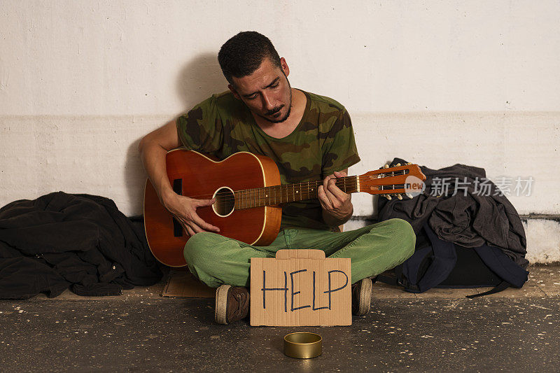 无家可归的街头艺人正在城市地下弹奏吉他，等待捐赠