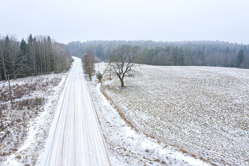 树林间的乡间小路和覆盖着积雪的农田。鸟瞰图