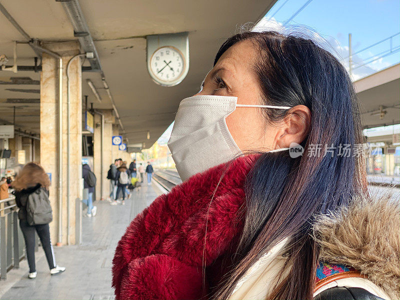 概念、疾病、病毒、过敏、空气污染。欧洲,意大利。中年妇女在车站戴着防护口罩等车